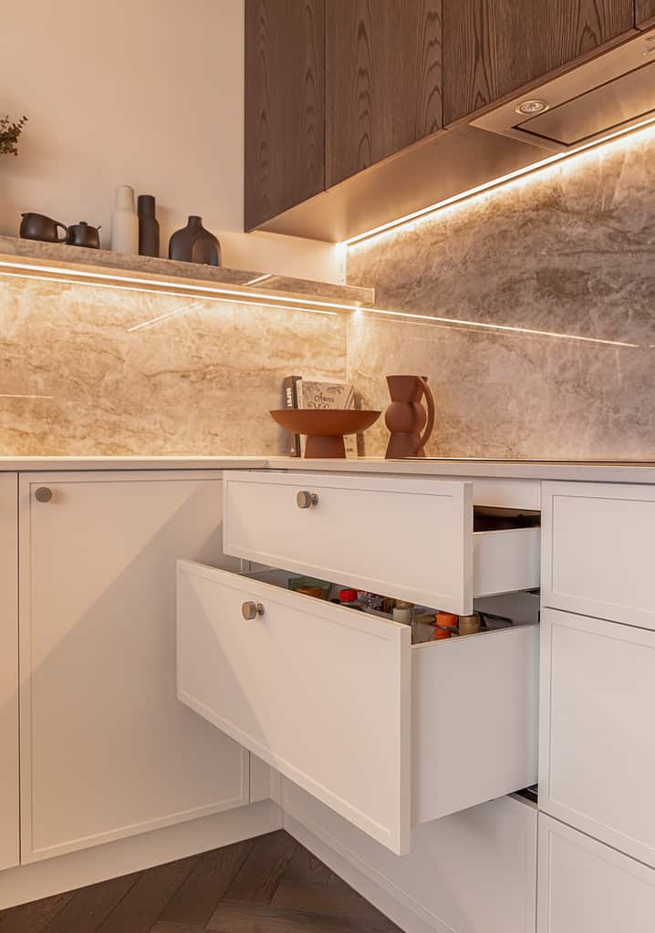 Cream AvanTech YOU cabinet drawers opened with marble splashbacks and dark oak upper cabinetry doors.