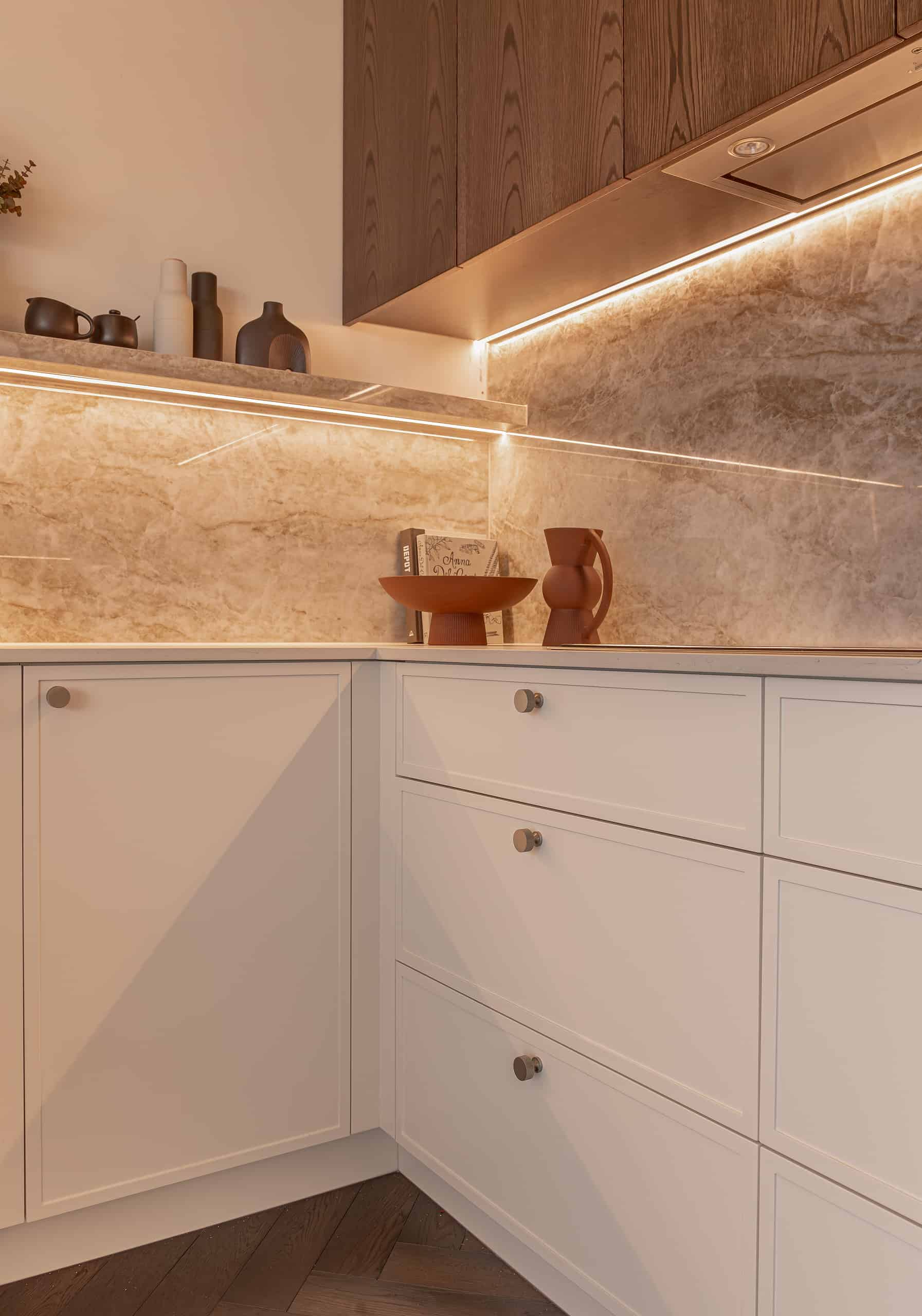 A cream kitchen with marble splashback, traditional cabinets closed and brown upper cabinetry