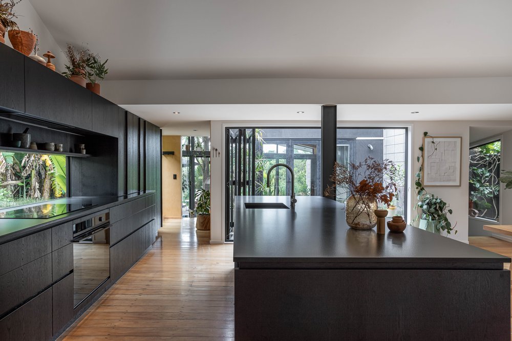 A charcoal stained wooden open plan kitchen with a black island bench that opens into the living room