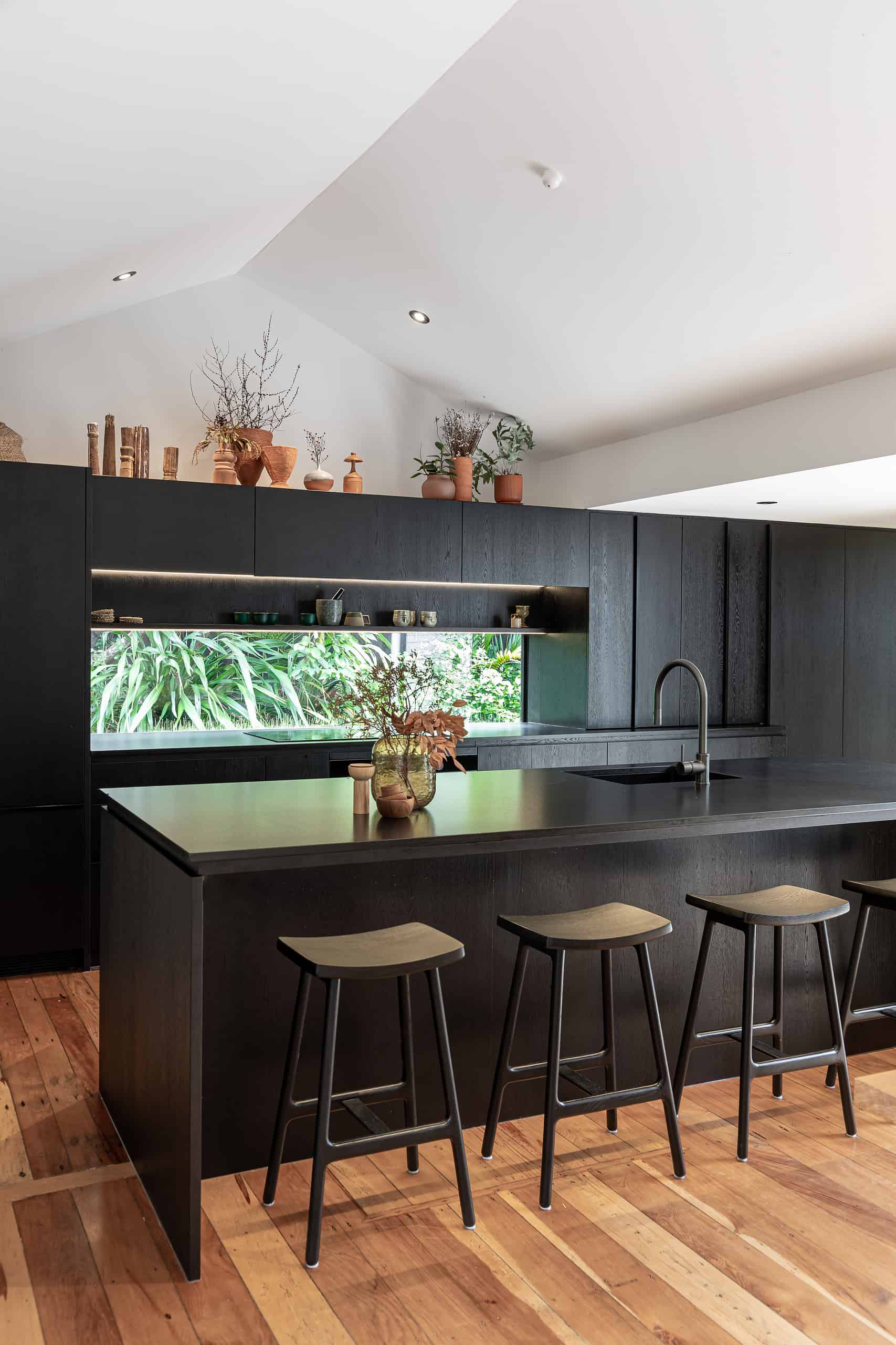 dark kitchen with black cabinetry and island benchtop greenery in view 