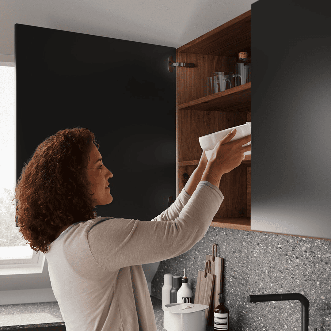 Women puts away bowls into cabinet door with sensys obsidian hinges